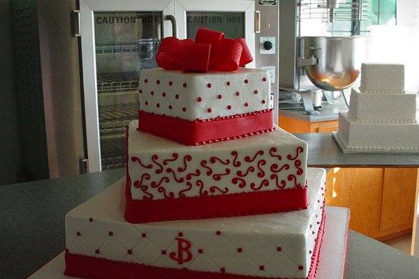 Three tier buttercream with red dots and swirls with fondant bands and bow.