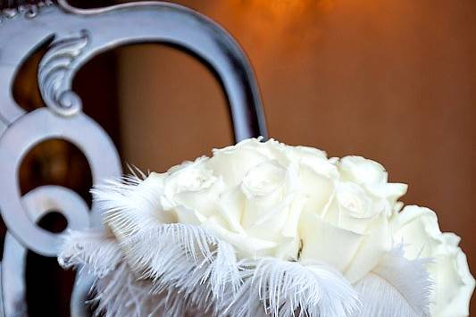 White roses are adorned with rhinestones and accented with white feathers. A crystal band is fastened around the ribbon.