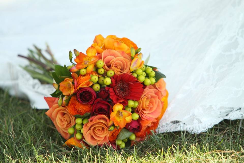Orange and red roses with hypericum berries make this bridal bouquet perfect for an outdoor fall wedding