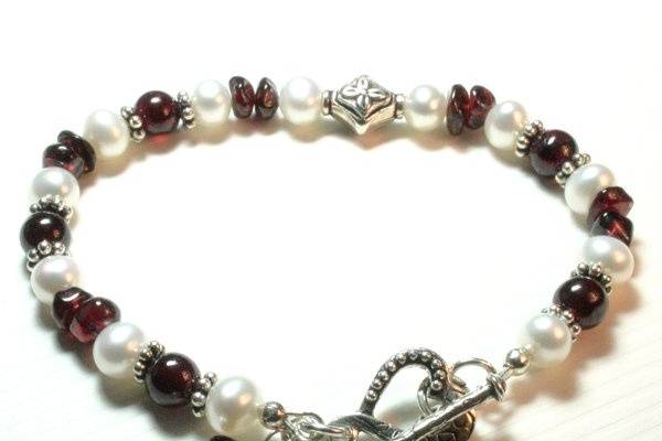 Heart's Desire BraceletA circle of white freshwater pearls alternate with round garnets and garnet chip beads, accented with Bali-style sterling spacer beads and one perfectly placed sterling flower bead.The closure is a sterling silver heart toggle clasp with a couple of flirtly charms- one matching the bracelet beads, the other a cute little sterling heart.All silver components are sterling silver.- 7 1/2