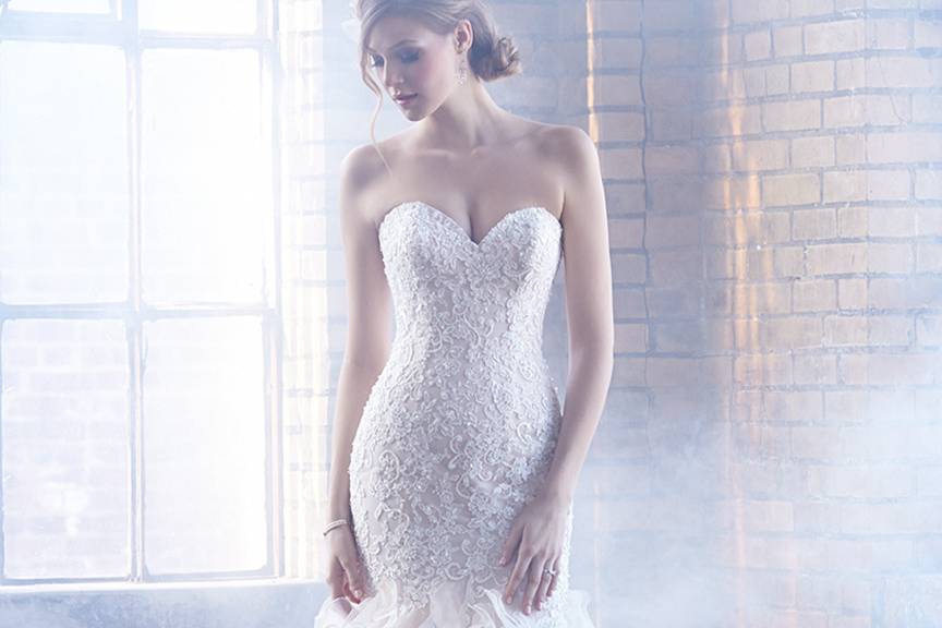 Style MJ155 <br> Textured lace embroidery trails down this gown to a dramatic ruffled skirt.