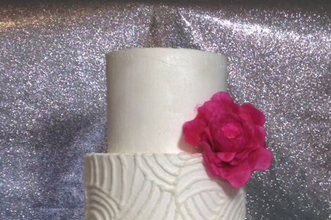 This 4-tier pearl white cake is decorated in all buttercream.  It has clean curvy piped lines, romantic wording, and large rosettes accented with silver.  We added a pop of color with a warm pink fantasy flower.