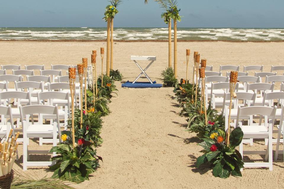 Tropical Bamboo beach wedding arch and aisle decor.  Tiki torches with fresh tropical flowers.  Orchid accents and lush foliage lining the aisle.  Beach weddings in Rockport and Port Aransas TExas