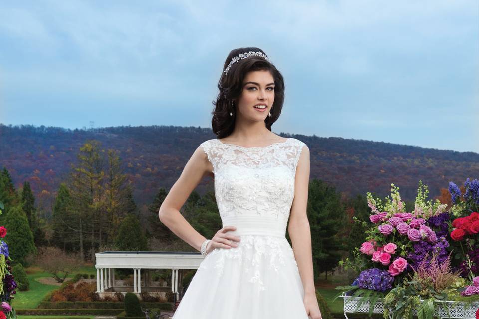 Style # 3804
Venice beaded lace over tulle ballgown with a boat neckline and pleated tulle cummerbund at the natural waist. The gown is finished with a V-back, tulle covered buttons to the bottom of the cummerbund and a chapel length train.