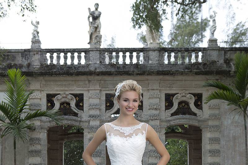 Style 3884 <br> This classic A-line gown features an illusion Sabrina neckline with beaded lace accents on the asymmetrically draped apron front skirt and corset back.