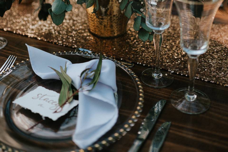 Wedding table details with a huge bouquet, glass plate and a gold runner, white napkin and a leaf
