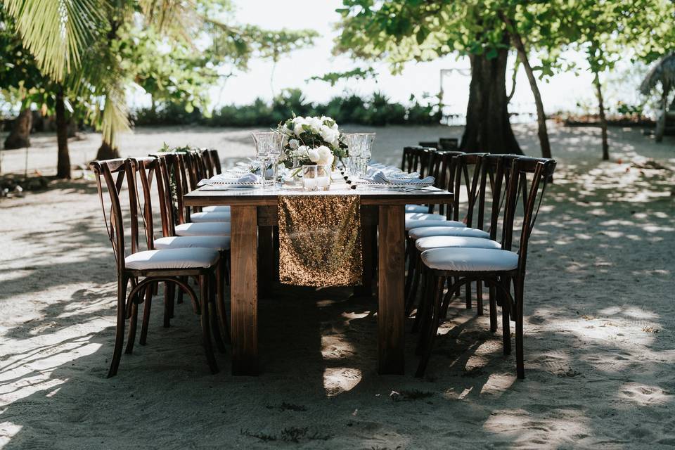 Beautiful wedding wooden table on the beach with X-back chairs and gold runner