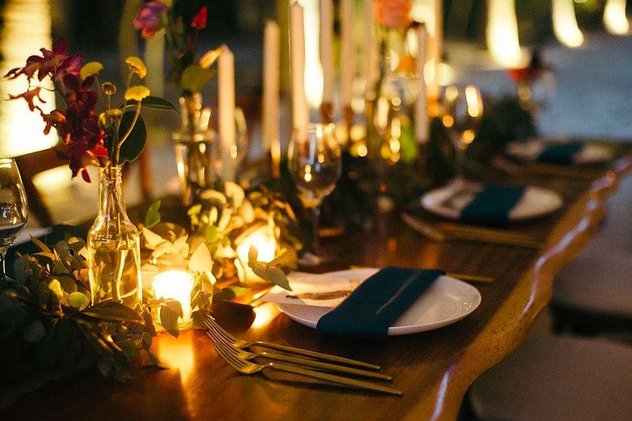 Wedding table centerpieces with copper pipe candleholders, greenery, flowers and blue napkins