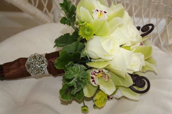 green cymbidium orchids with white roses, lime green button mums, brown monkey tail, scented geranium, brown satin ribbon with antique brooche.