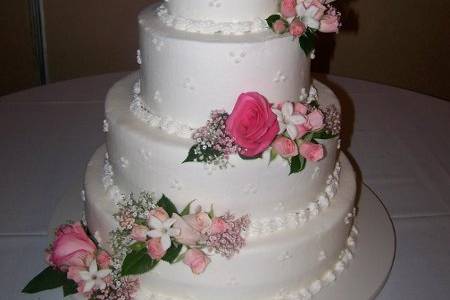 A 4 tier strawberry cake with strawberry filling. Soft pastel flowers adorn the cake in a light cascade.