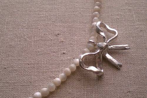 Hand sculpted sterling silver bow sits off center on a strand of faceted mother of pearl.
The necklace measures 15 1/2