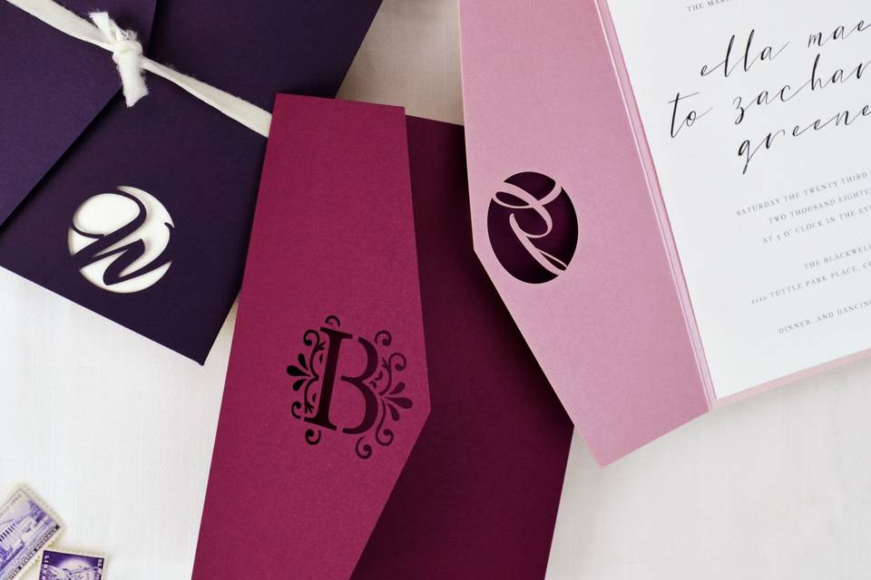 Laser cut monogram pockets to personalize your wedding invitations. Shown in Amethyst, Burgundy, and Misty Rose.