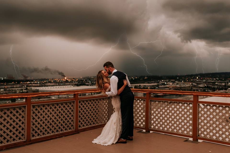 Newlyweds kiss against a stormy sky