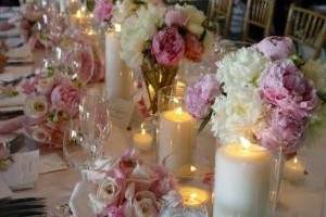 Peonies and roses in hues of pink and white in clear vase. Lining the table with huge pillar candles in a warm vanilla sugar scent. The bride and groom used the scented candle (which is not always advised) since their first date was to a candle maker where they created a warm vanilla sugar scented candle. This personal touch added personality and brought the guest into the heart of this union.