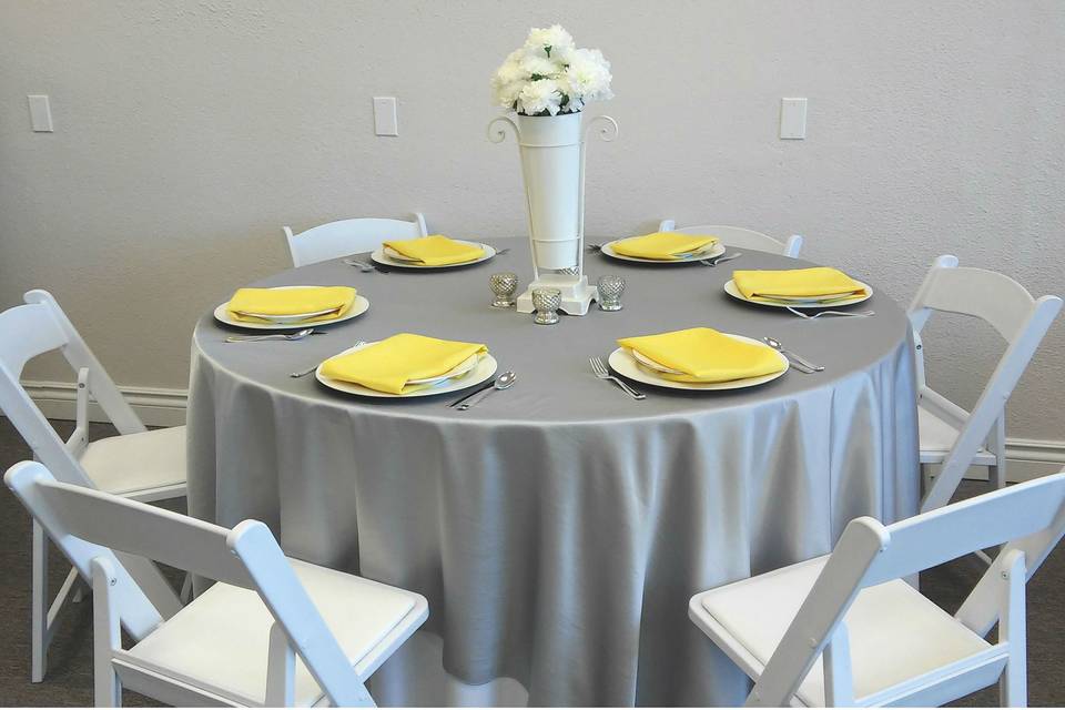 Silver dupioni table cover, white charger plate, white and silver china, lemon yellow napkin. Resin folding chairs. All available at Lake Party Rentals, Osage Beach, MO.