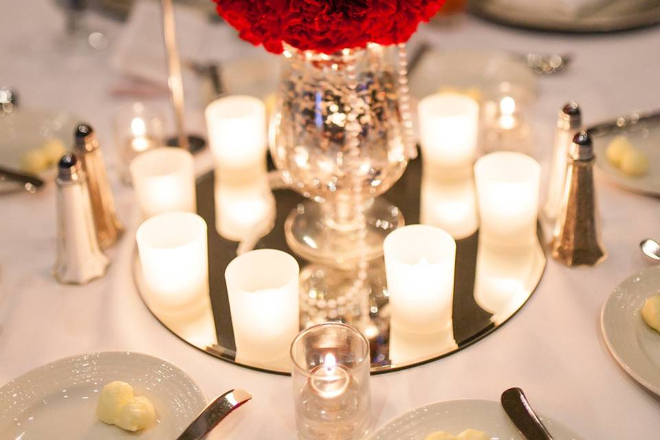 Amazing red carnation ball is sitting on a mercury glass vase with pearls and frosted votives.