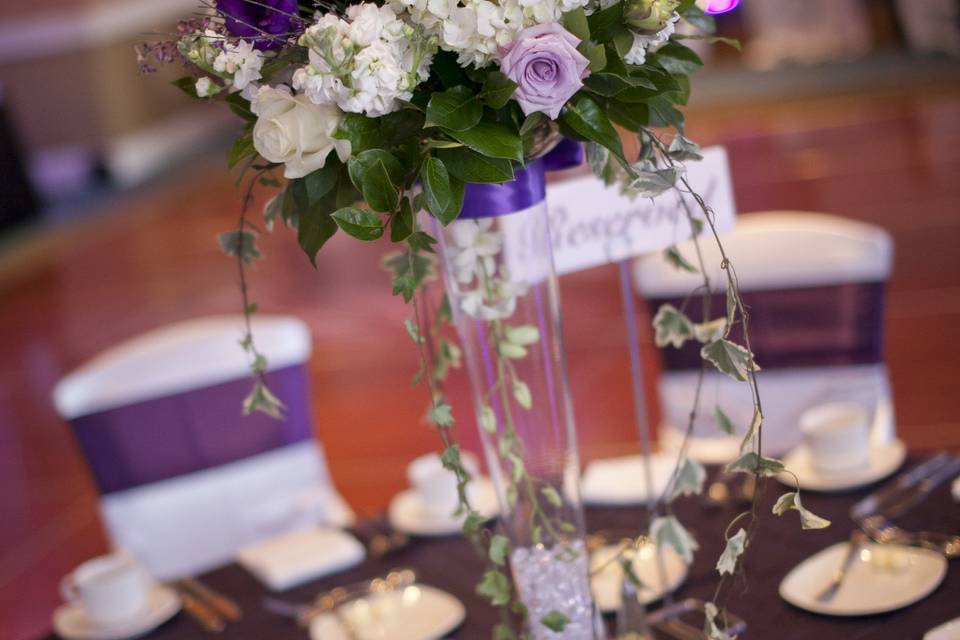Tall centerpieces in glass vases with purple lisianthus, lavender roses and white hydrangea with greens and ivy.