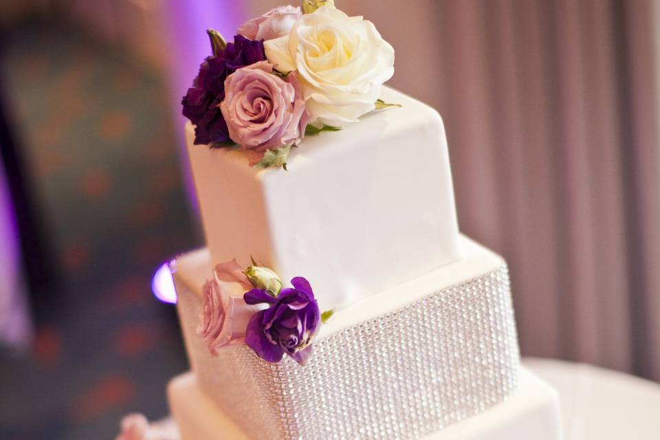 Cake adorned with bling and white lavender roses with purple lisianthus.