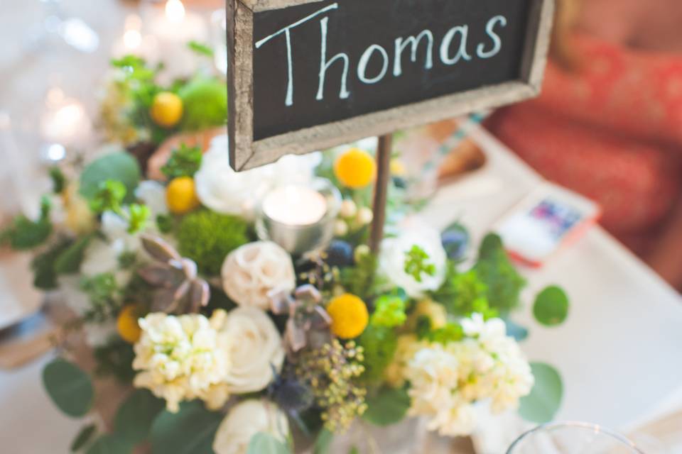 Low centerpieces in white washed wood boxes complete with chalkboard sign featured tall tea light candles and a wildflower vibe complete with raffia balls.