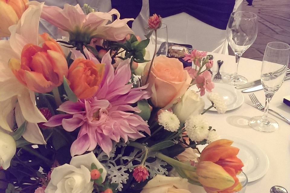 Airy low centerpiece in pale shades of orange, peach, pink and ivory.  The arrangement included dahlias, roses, tulips, ranunculus and greens.