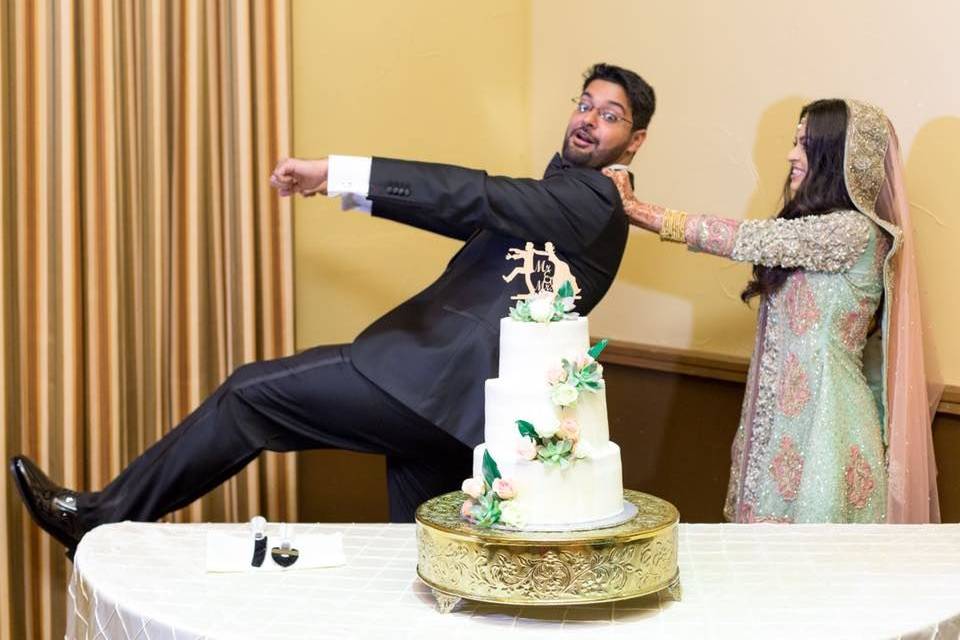 Newly-weds have fun by the wedding cake