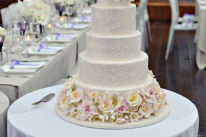 Ana Parzych Custom CakePink pearlescent fondant tiers embellished with a brushed embroidered flower design.Top and bottom tiers feature hand-crafted sugar flowers in pastel colors.