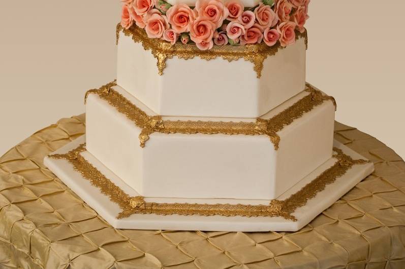 Ana Parzych Custom CakesHexagon white fondant tiers embellished with pressed fondant borders finished with edible gold. Featuring a gold monogram and sugar roses in peach shades.