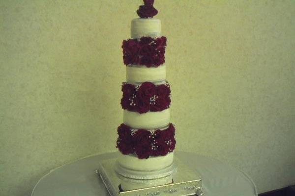 Four Tiered cake with red velvet roses nestled between each tier. Cake displayed on a sterling silver cake plateau.