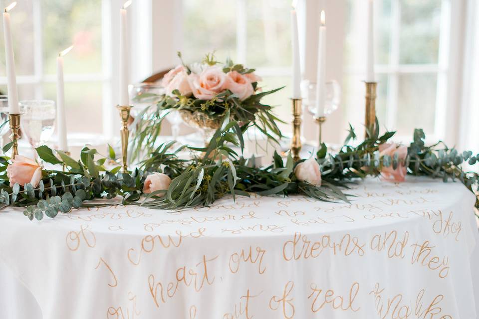 The sweetheart table was adorned with a cascading floral garland, gold flatware and a table linen with gold hand calligraphy with Jack Johnson song lyrics.