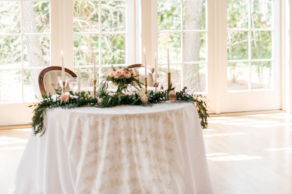The sweetheart table was adorned with a cascading floral garland, gold flatware and a table linen with gold hand calligraphy with Jack Johnson song lyrics.