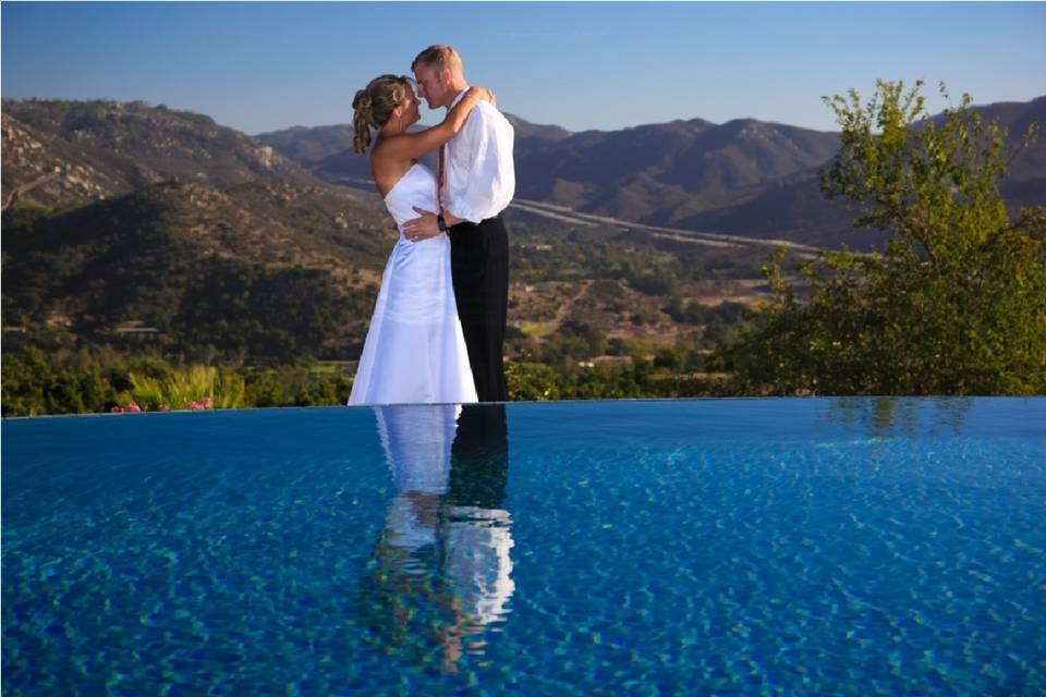 Couple embracing as if to dance, but with their gorgeous reflection in an edgeless pool, with a fantastic valley view behind them