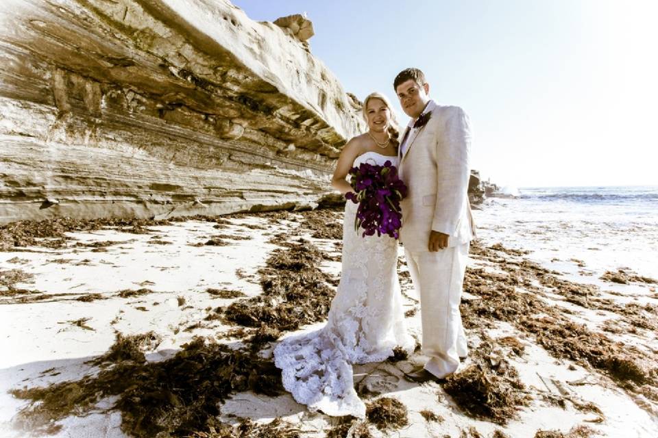 Couple on beach, both in white, dramatic sea wall and ocean behind them