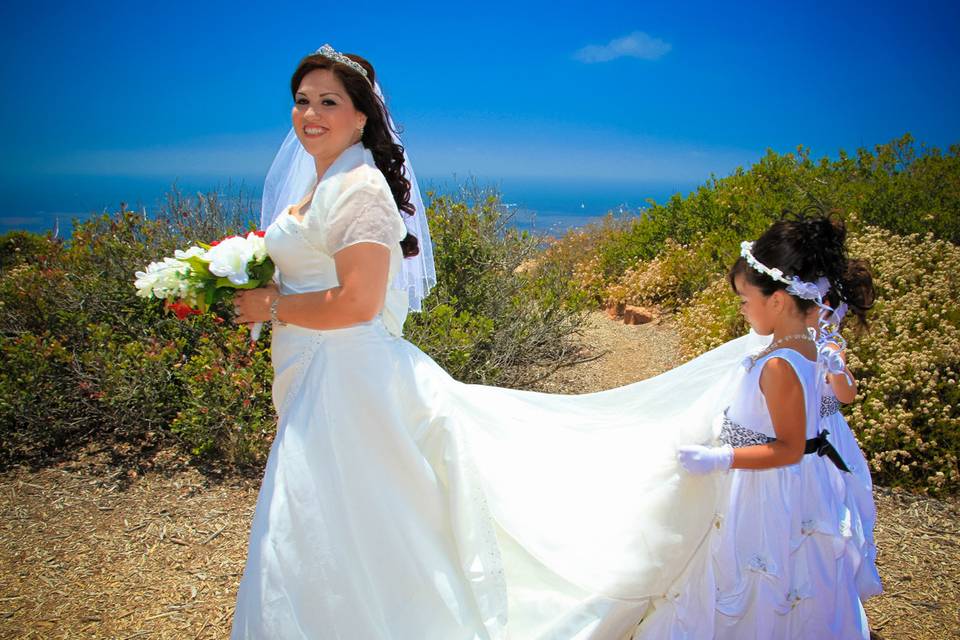Bride with dress train being carried by flower girls, blue ocean in the background. Cabrillo National Monument, San Diego, CA.