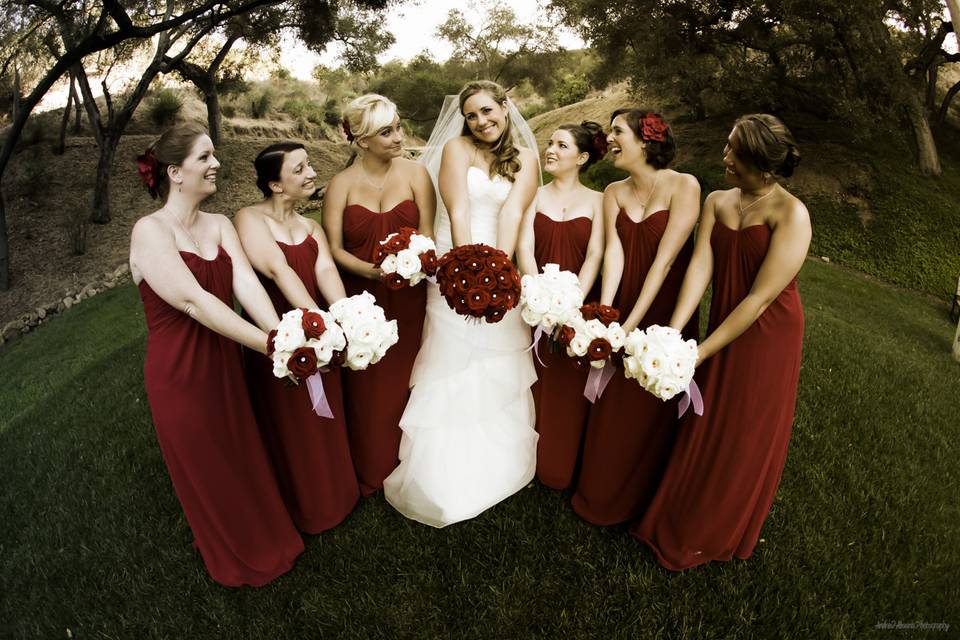 Bride in white with her bridesmaids in red, all holding their bouquets together