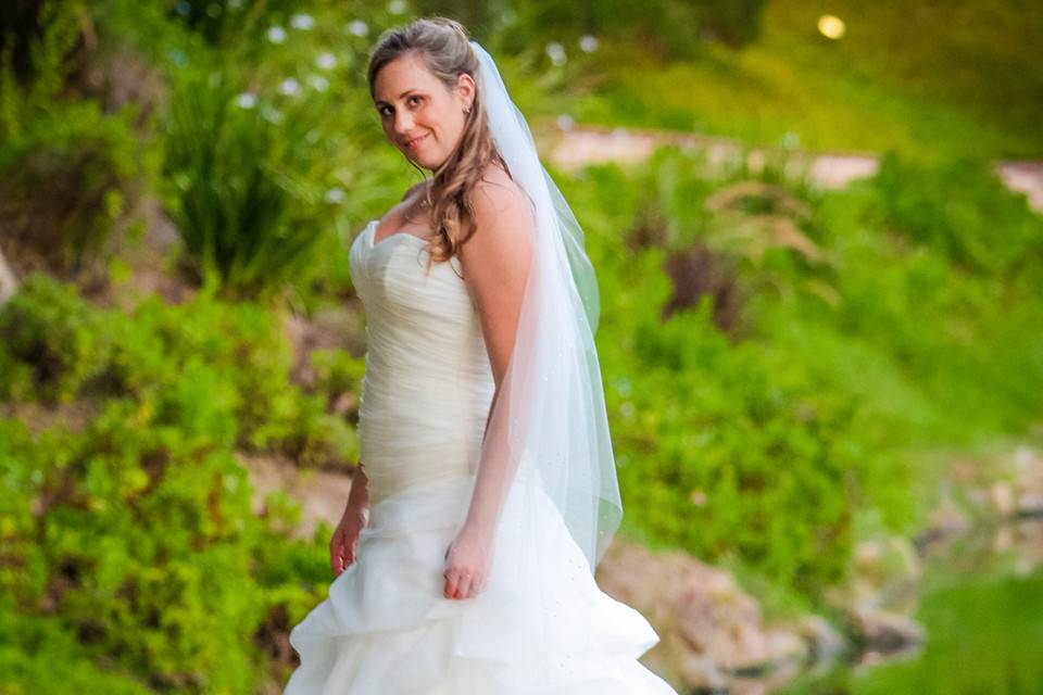 Bride on ledge above reflecting pool with greenery behind her