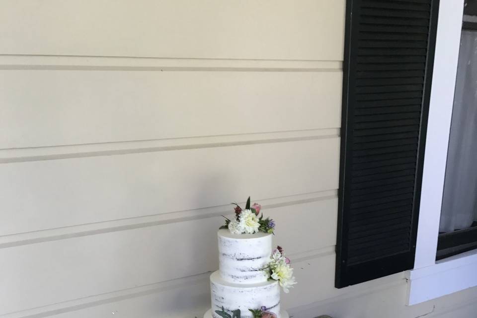 The naked style cake on a rustic stand in a beautiful setting.