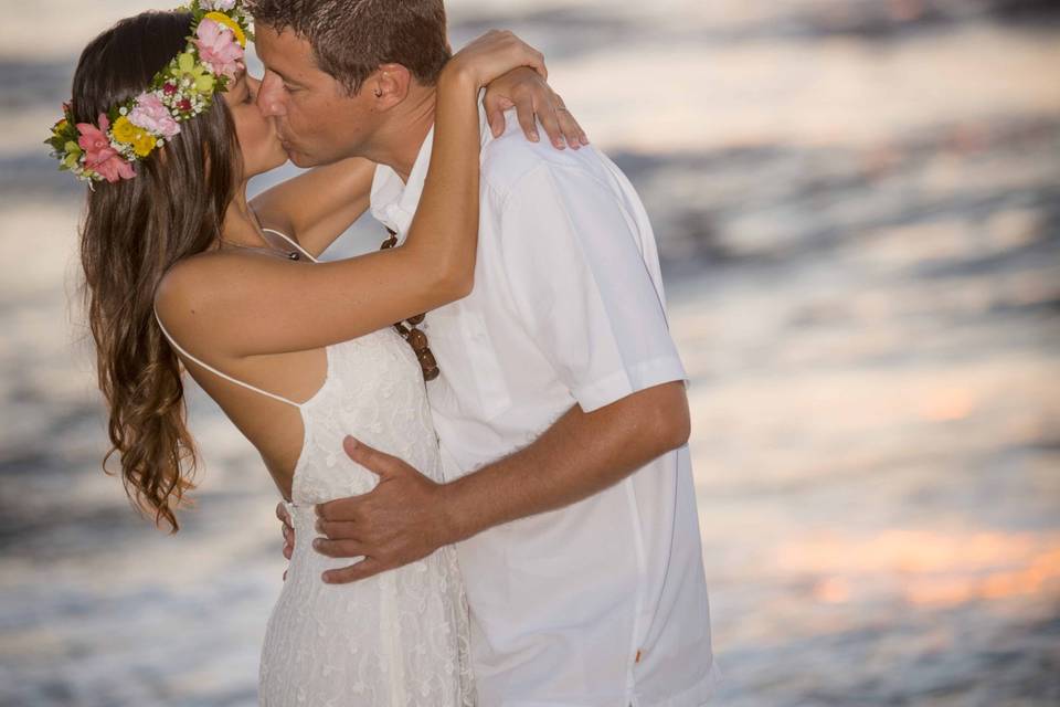 Simple sunset beach wedding on the island of Oahu at the famous north shore. She is wearing a Haku Lei with a summer length dress and he is in a simple white oxford with Khaki shorts, barefoot on the beach in Hawaii