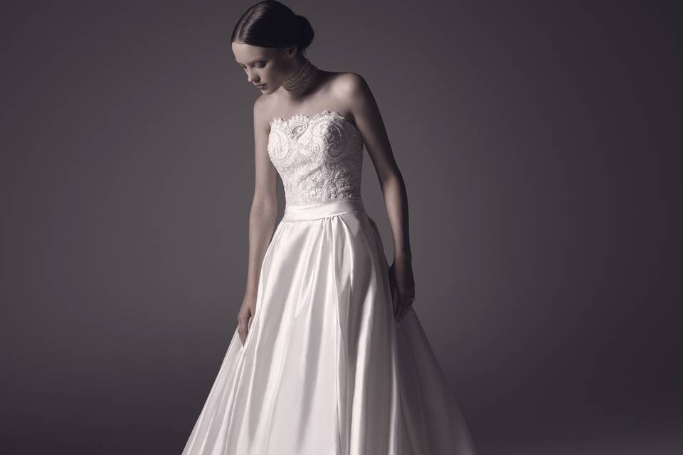 Style C106 Rhea  Rhea’s classic a-line silhouette features an exquisite bodice with a straight across neckline brimming with beaded lace appliques that perfectly complement the buttery silkiness of the full skirt.