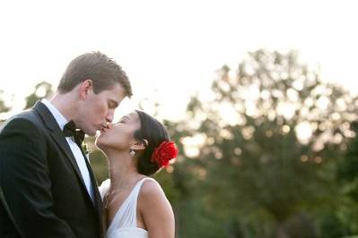 With a crimson flower, the bride shares a sweet moment with her new husband in the setting sun.