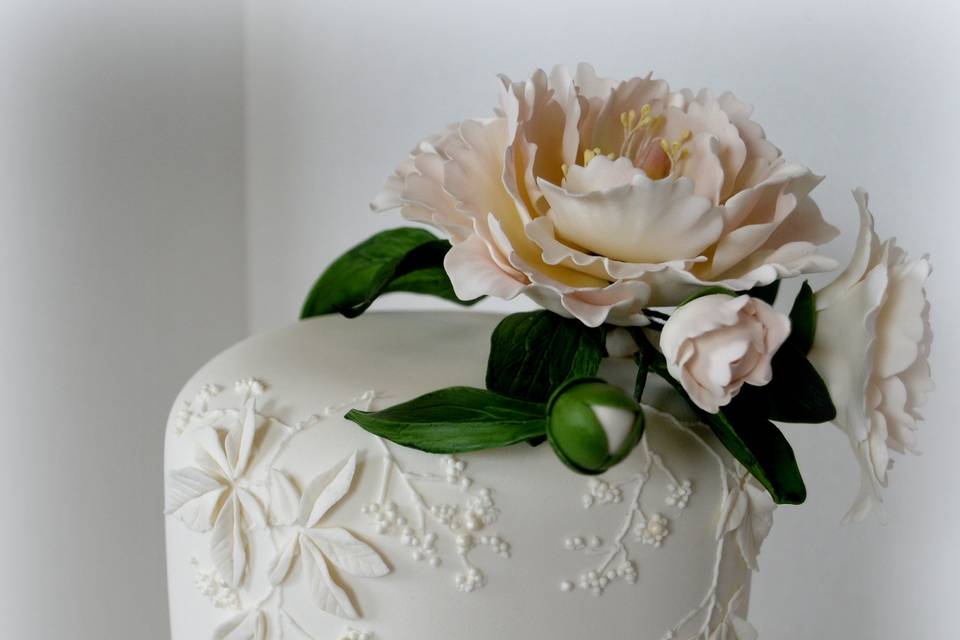 White on white bas-relief wedding cake with botanical appliques and handcrafted blush pink sugar peony.