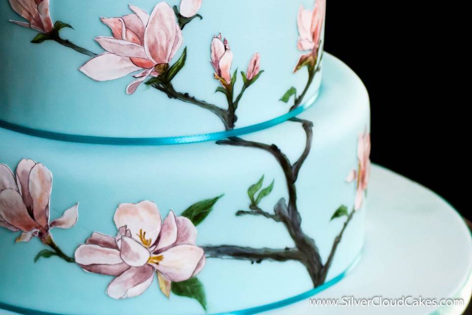 Bridal shower cake with handpainted magnolia blossoms and two love birds in cocoabutter with sugar wedding rings.