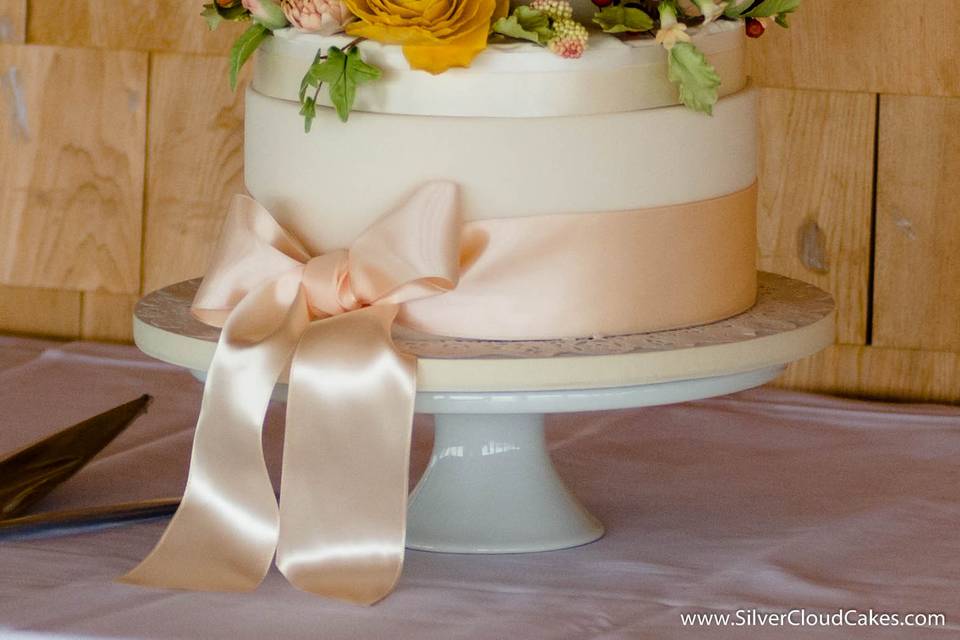 A wreath of handsculpted sugar flowers circles this beautiful wedding cake.