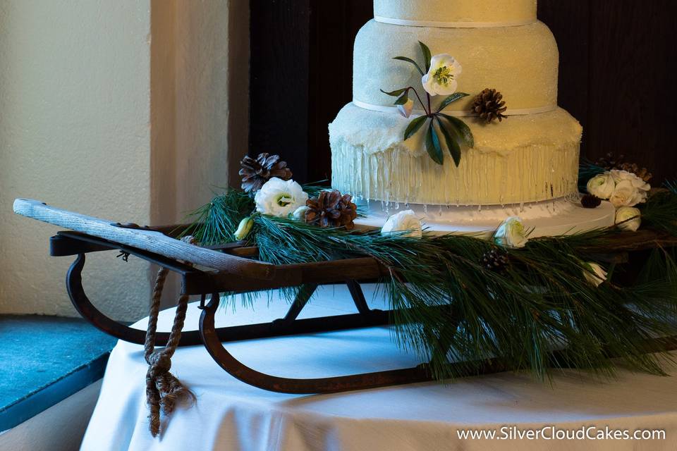 A winter wedding cake perches on an old wooden sleigh.  Carrot Cake with White Chocolate Cream Cheese Buttercream.