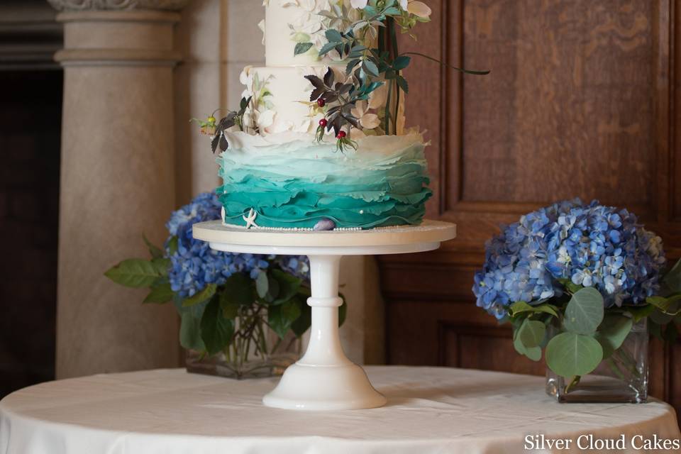 Handcrafted beach roses pose above ombre waves on this beach theme wedding cake. Bas relief rose leaves and handpainted cocoa butter details add texture to this exquisite cake.