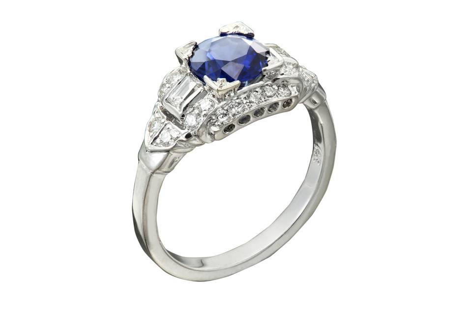 A classic engagement ring with a round sapphire center stone. Around the sapphire there are both round and straight baguette diamond accents.