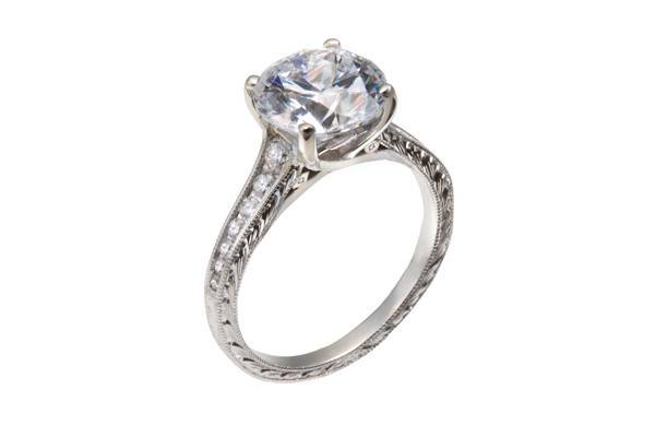 A lady's vintage and diamond engagement ring with a round diamond center stone, round diamond accents, and hand engraving.