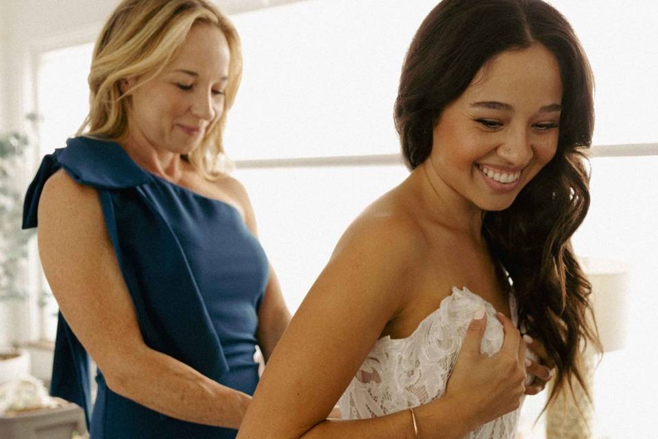 Mom zipping up bride