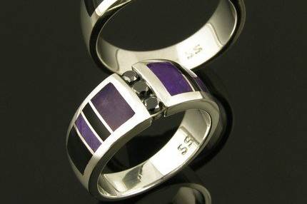 Unique his and hers sterling silver black diamond wedding set inlaid with sugilite and black onyx. Matching handmade bands feature 3 channel set round black diamonds flanked by alternating black onyx and purple sugilite inlay. His wedding ring has 3 black diamonds totaling .24 carats. The ring is 9.5mm wide and is a size 10 1/2. This band is available in other sizes and color combinations by special order. It is hand signed 