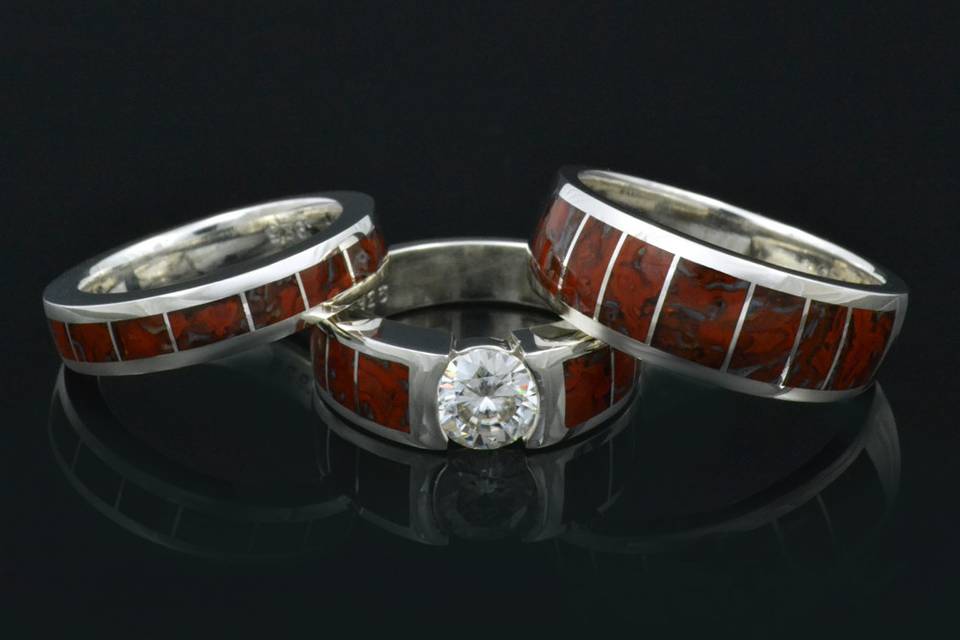 Dinosaur bone wedding ring set featuring a brilliant round moissanite in the engagement ring.  All the rings are in sterling silver inlaid with matching red-orange dinosaur bone.  This set is also available with other center stones and inlay materials by special order.  This set will be made to order in your ring sizes in 3 to 6 weeks.