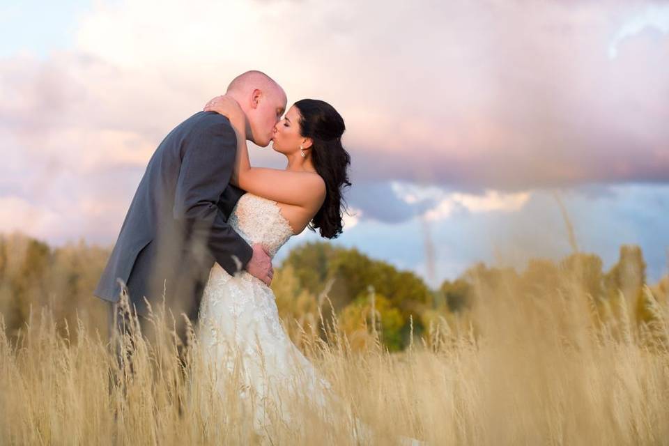 Couple kissing in a field with tall grasses, portrait taken by Lovely Day photo